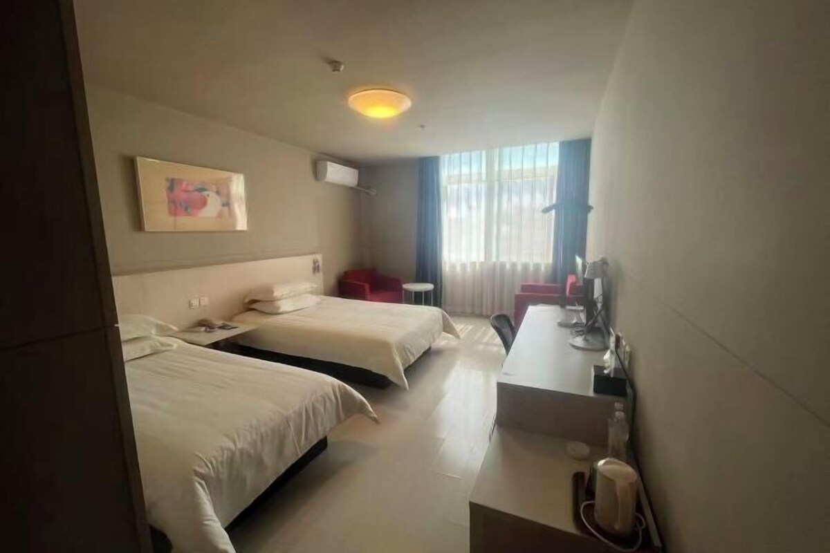 A hotel room with two beds, a desk, a chair, a TV, and a window with curtains.