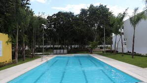 A rectangular swimming pool with clear blue water, surrounded by a concrete deck and a grassy area with trees. - Casa Vacacional Brothers House Economica (Playa del Carmen)