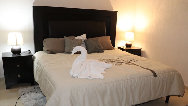 A neatly made bed with a swan towel centerpiece, two bedside lamps, and a dark headboard. - Casa Vacacional Brothers House Economica (Playa del Carmen)