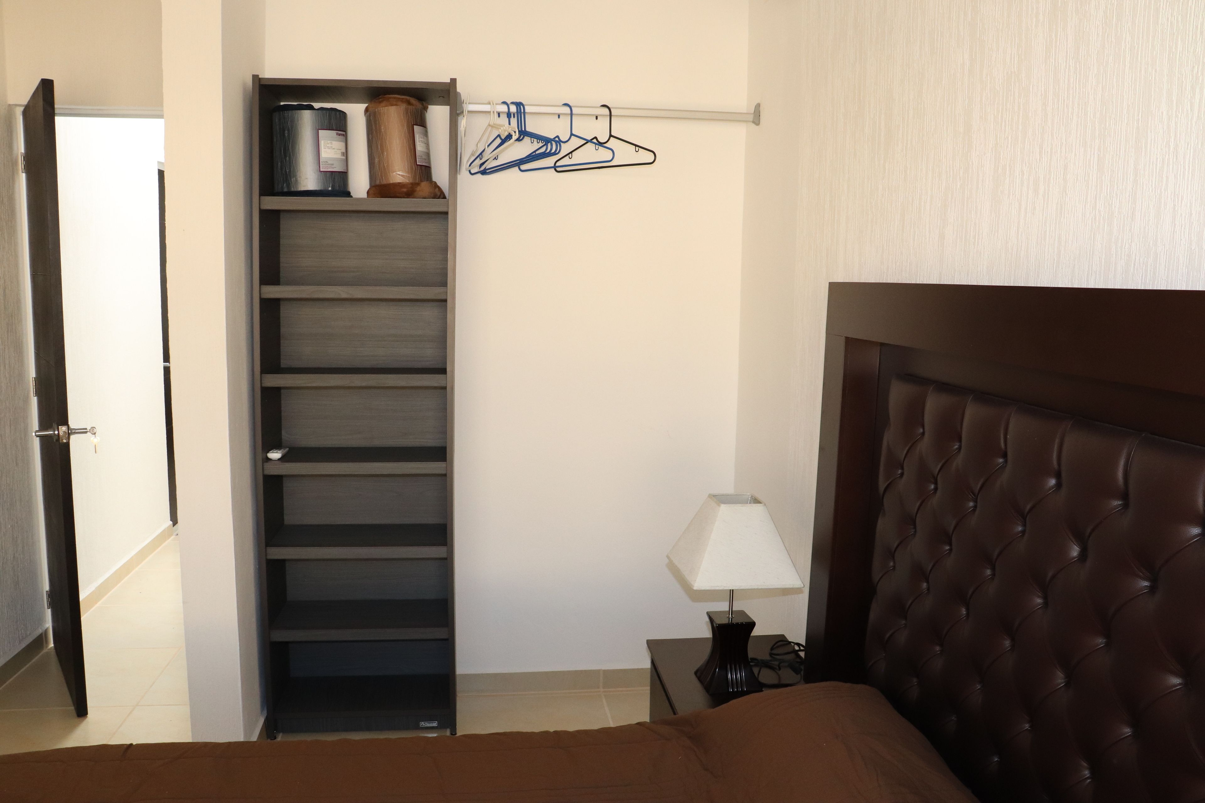 A bedroom with a bed, a nightstand with a lamp, a wardrobe, and a door.