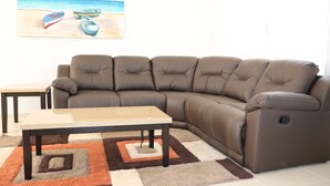 A brown leather sectional sofa, a wooden coffee table, and a patterned rug in a living room with a painting of boats on a beach. - Casa Vacacional Brothers House Economica (Playa del Carmen)