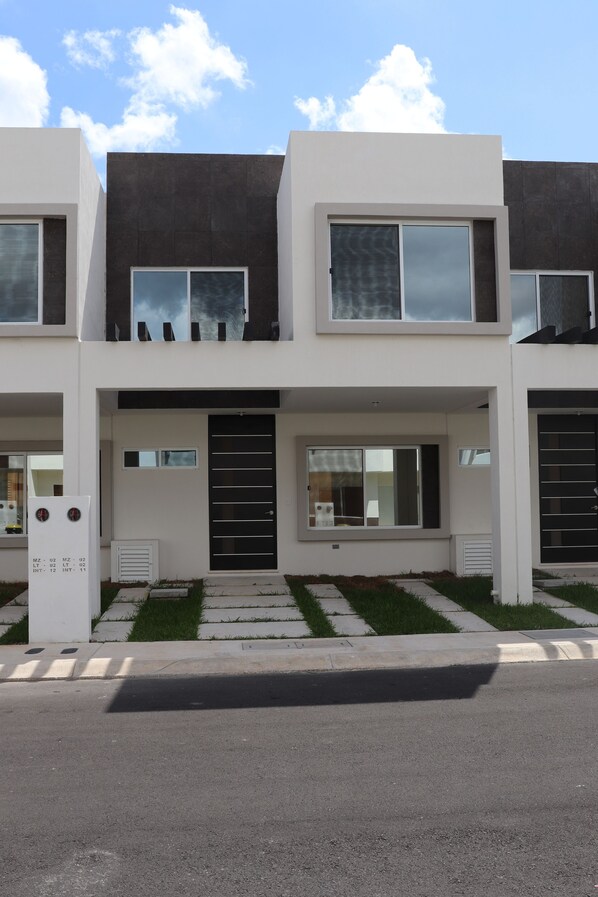 A modern two-story house with a flat roof, large windows, and a front door.
