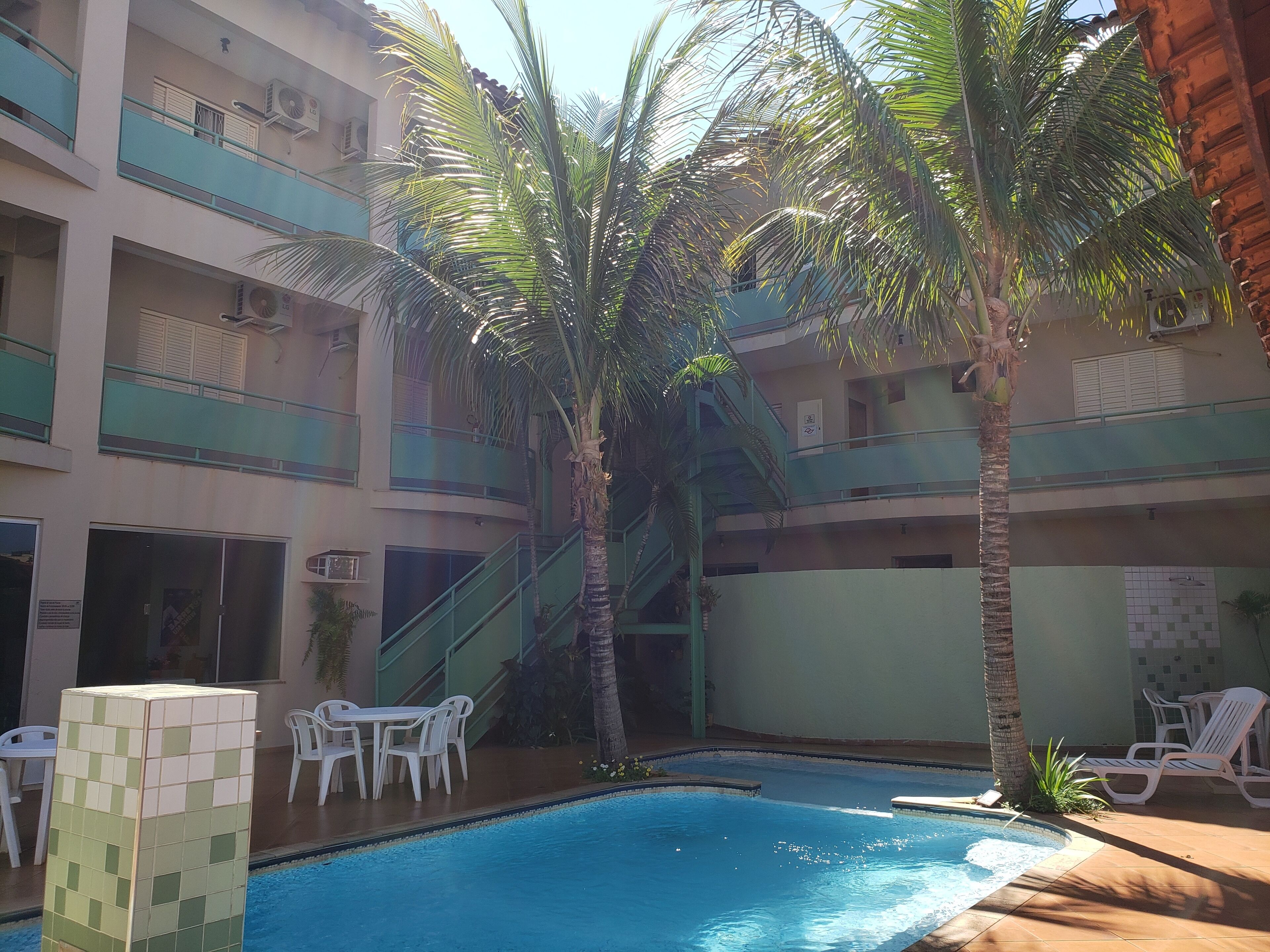 A pool area with a tiled structure, lounge chairs, and palm trees.