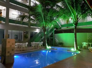 An indoor swimming pool with palm trees, surrounded by white chairs and a staircase. - Proença Hotel (Barretos)