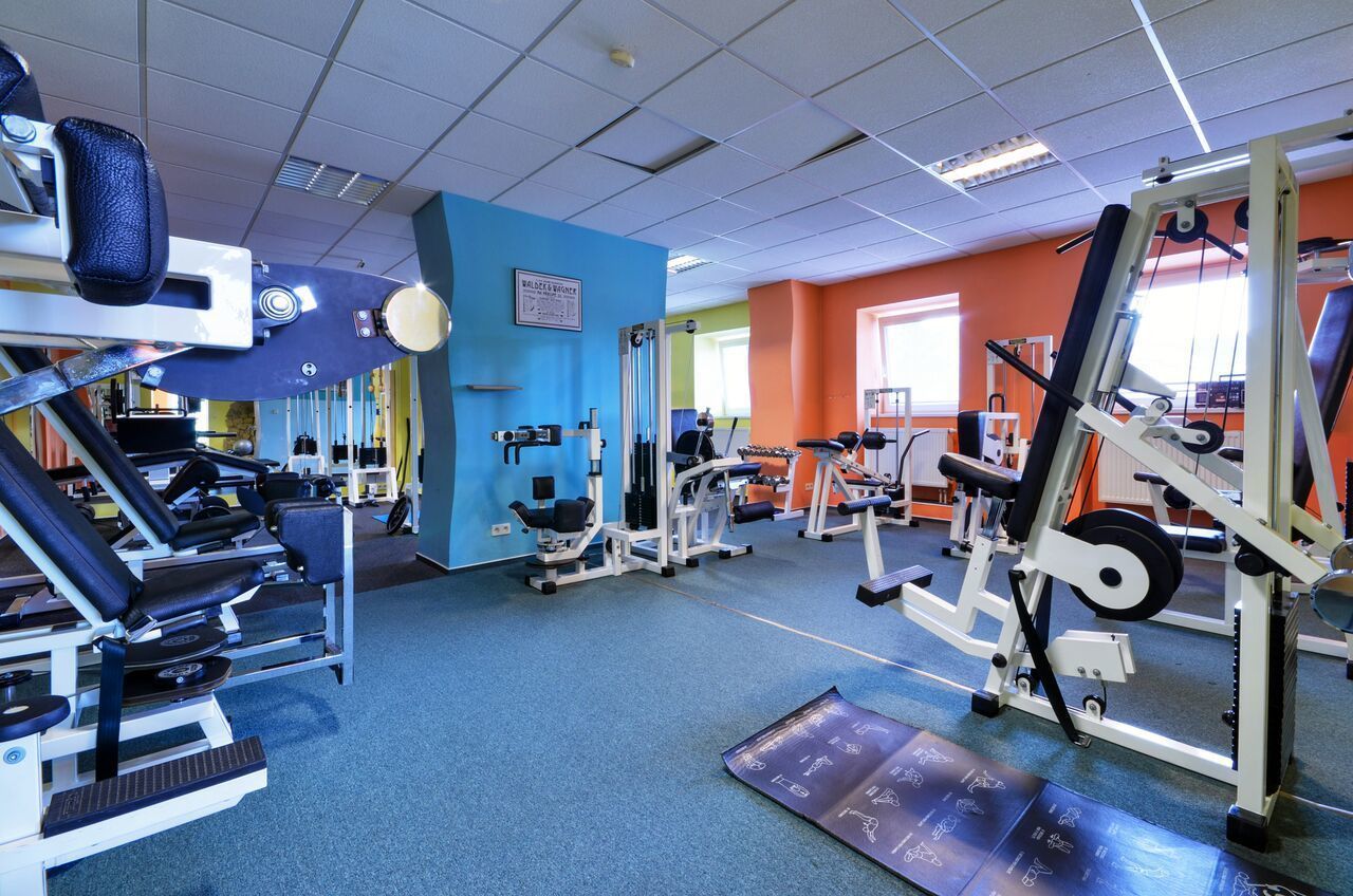 A gym with various exercise machines, a blue wall, and a colorful orange wall.