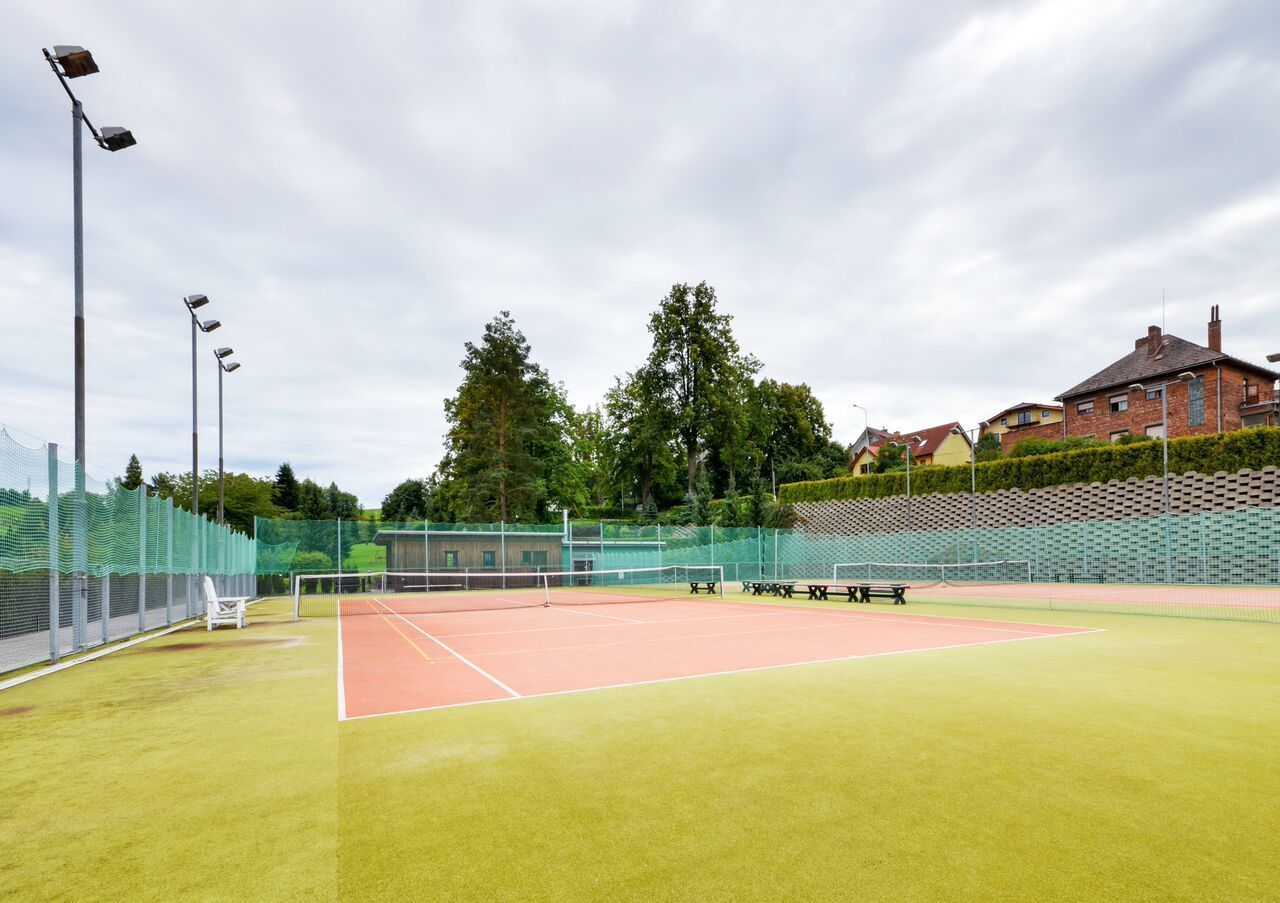 Una cancha de tenis exterior con red, bancos y valla.