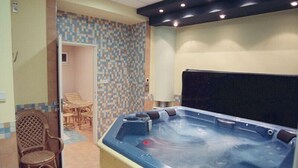 A spa area with a hot tub, wicker chairs, and a tiled wall. - Hotel Filipinum (Jablonne nad Orlici)