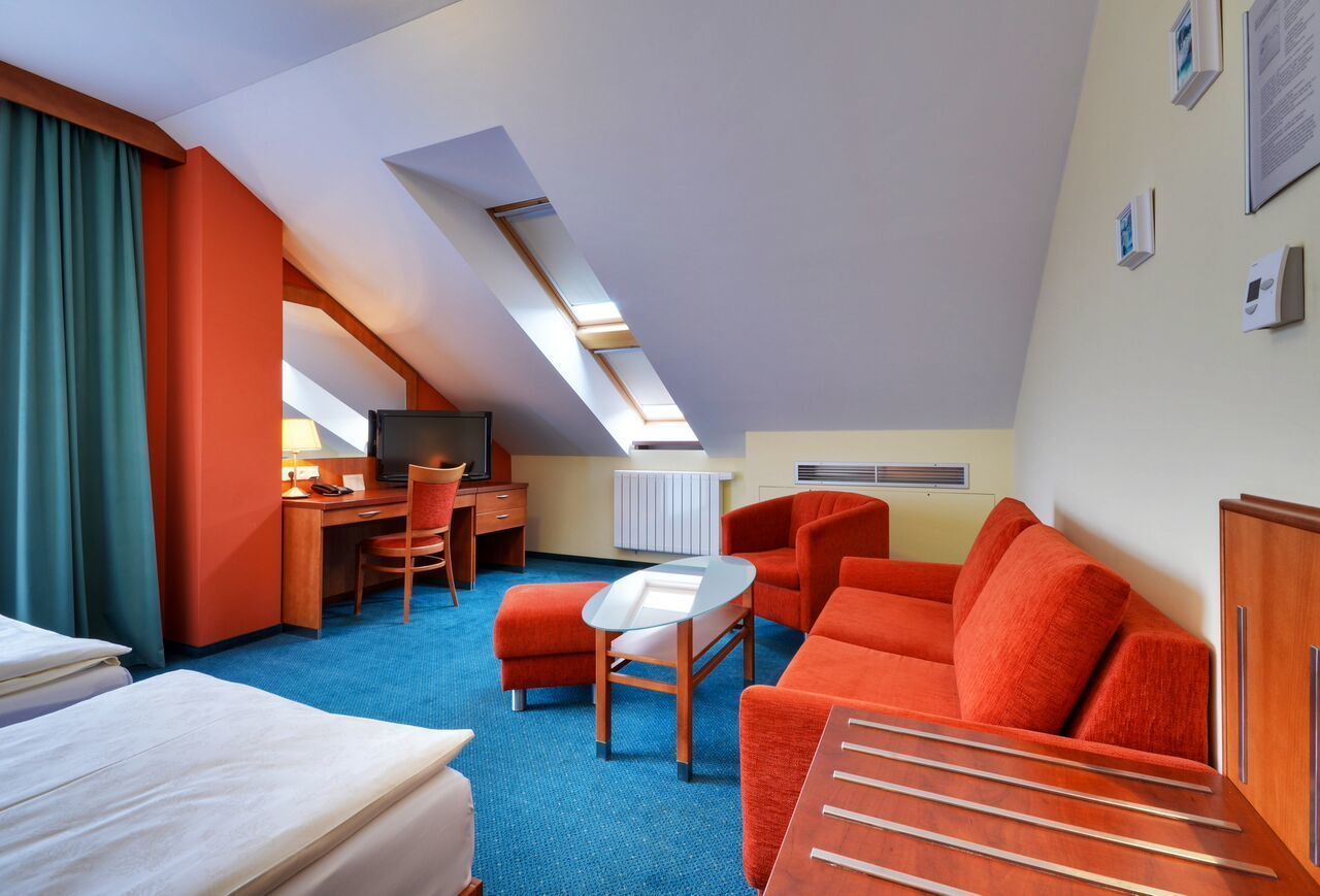 Ett hotellrum med ett sluttande tak, ett skrivbord med en stol, en soffa, en säng och ett litet bord.