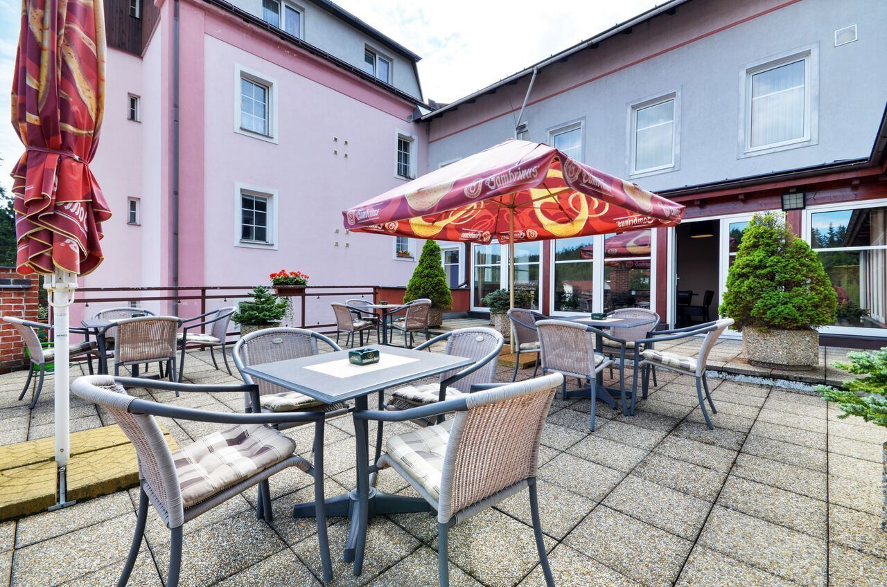 An outdoor patio with tables and chairs, a large umbrella, and a building in the background.