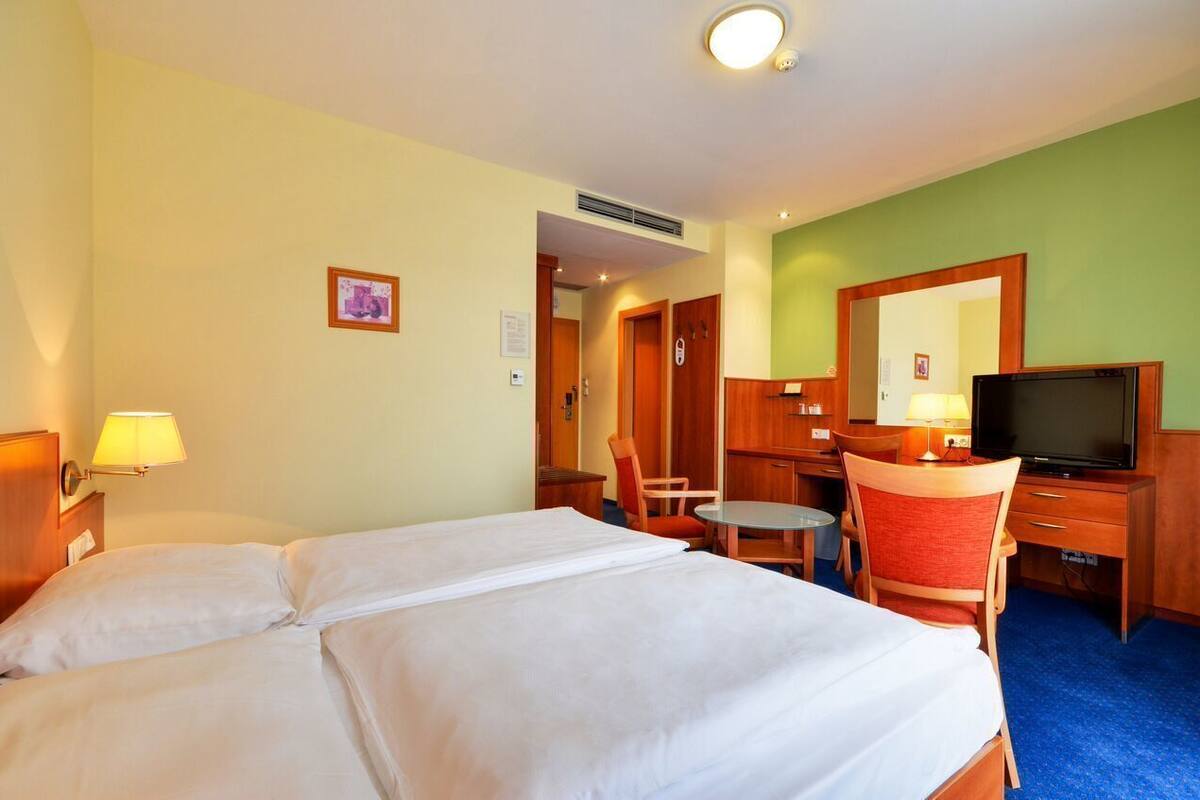 A hotel room with a bed, a desk with a chair, a television, and a mirror.