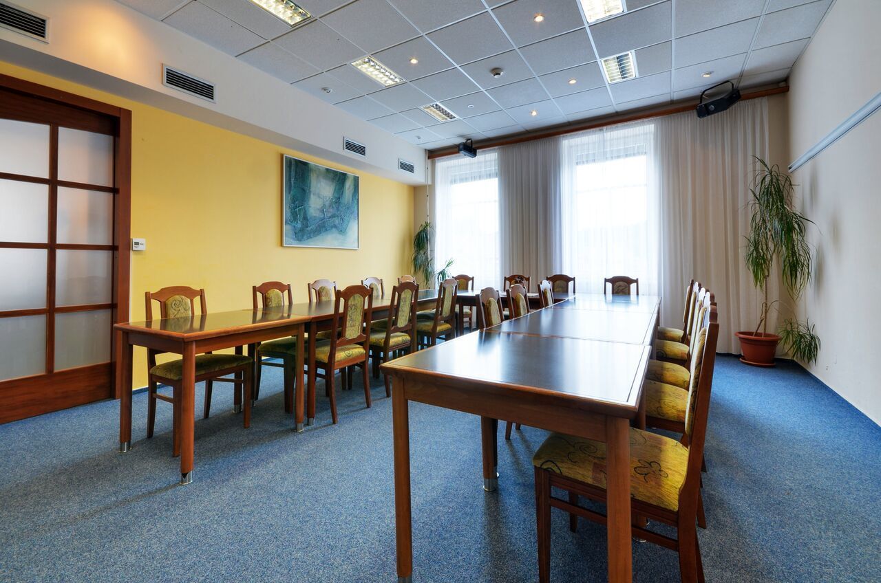 Un salón de conferencias con una larga mesa y sillas, ventanas grandes con cortinas y un cuadro en la pared.