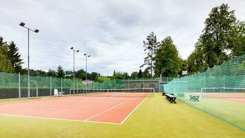 A tennis court with a net, floodlights, and seating areas.