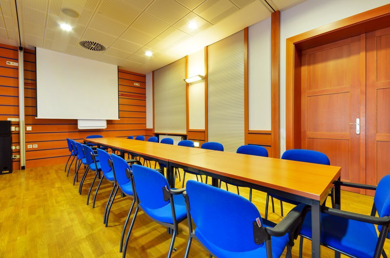 Una sala conferenze con un lungo tavolo, sedie blu, una lavagna e uno schermo per proiettore.