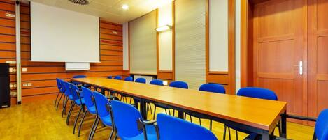 Una sala de conferencias con una larga mesa, sillas azules, una pizarra y una pantalla de proyector.