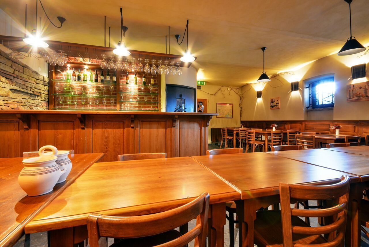 A restaurant interior with wooden tables and chairs, a bar area with bottles and glasses, and pendant lighting.