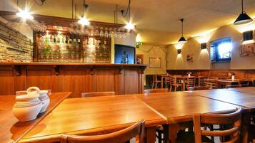 A restaurant interior with wooden tables and chairs, a bar area with bottles and glasses, and pendant lighting.