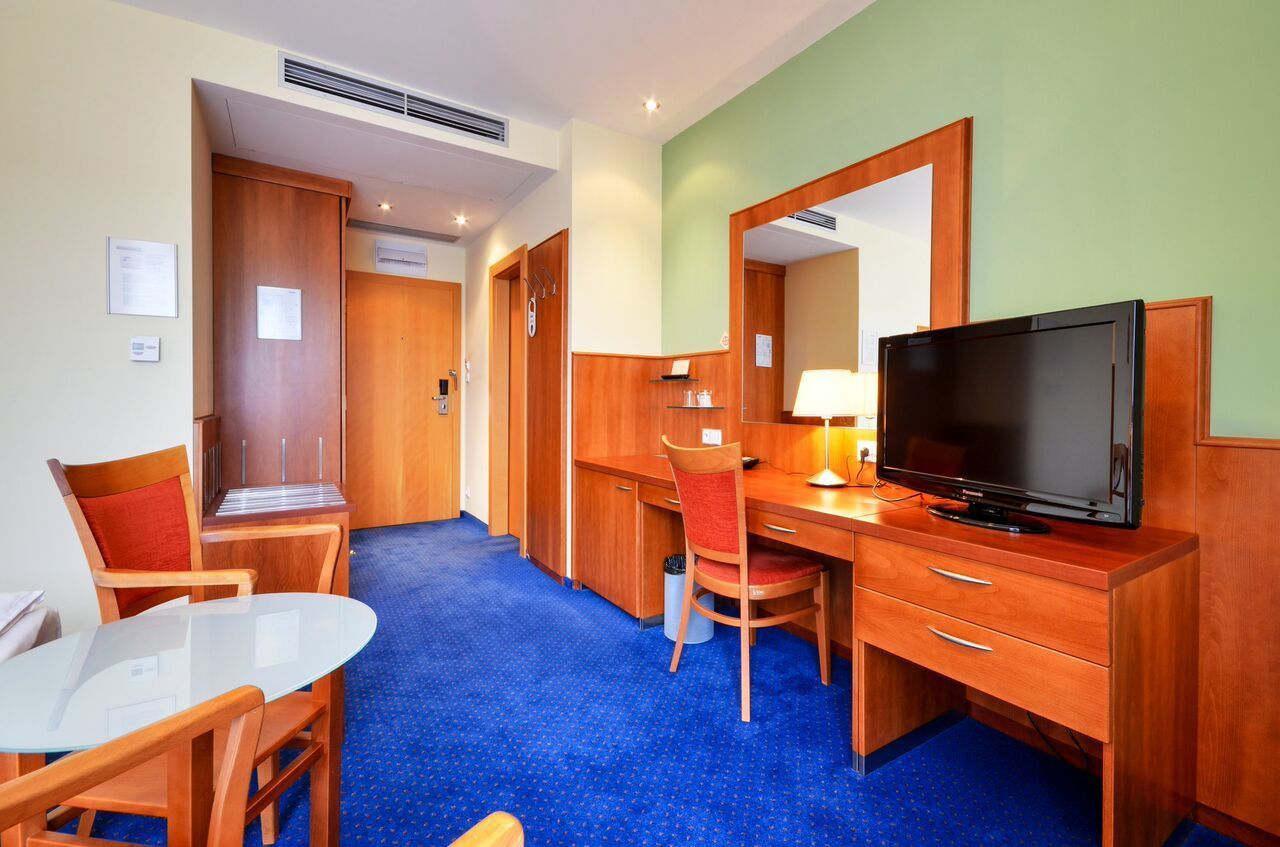 Een hotelkamer met een houten bureau, een televisie, een stoel, een tafeltje en een blauw vloerkleed.