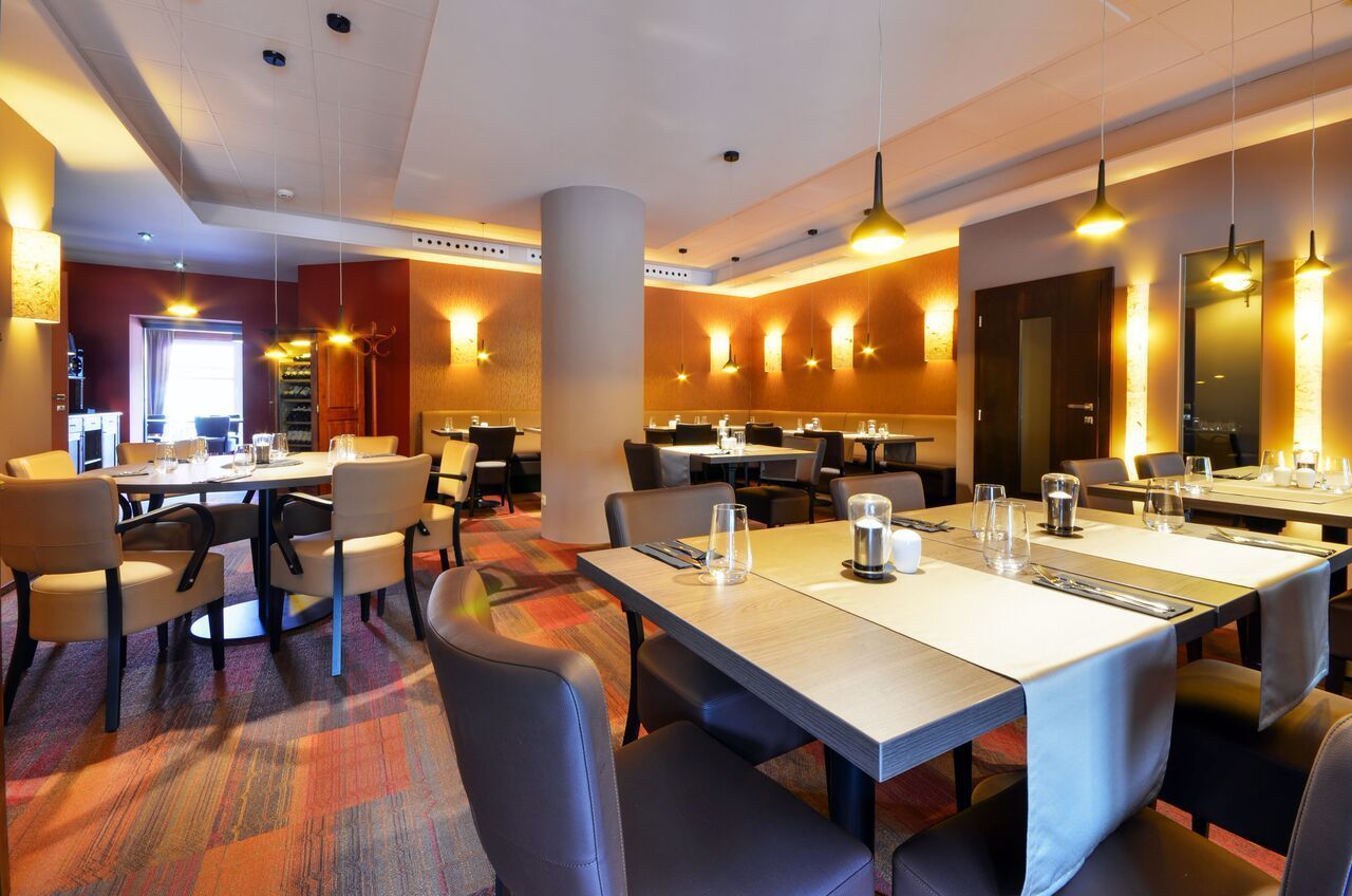 Une salle à manger d’hôtel avec plusieurs tables et chaises, un sol recouvert de moquette et des luminaires suspendus.