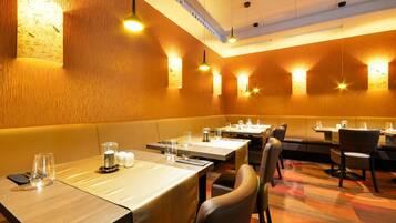 Un restaurante con cabinas y mesas, iluminación cálida y una alfombra estampada.