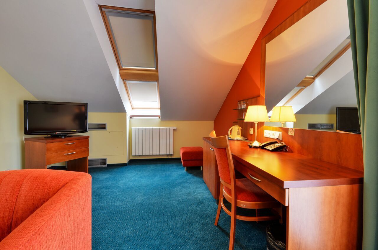 Une chambre d’hôtel équipée d’une télévision, d’un bureau avec un téléphone, d’une chaise et d’un canapé rouge.