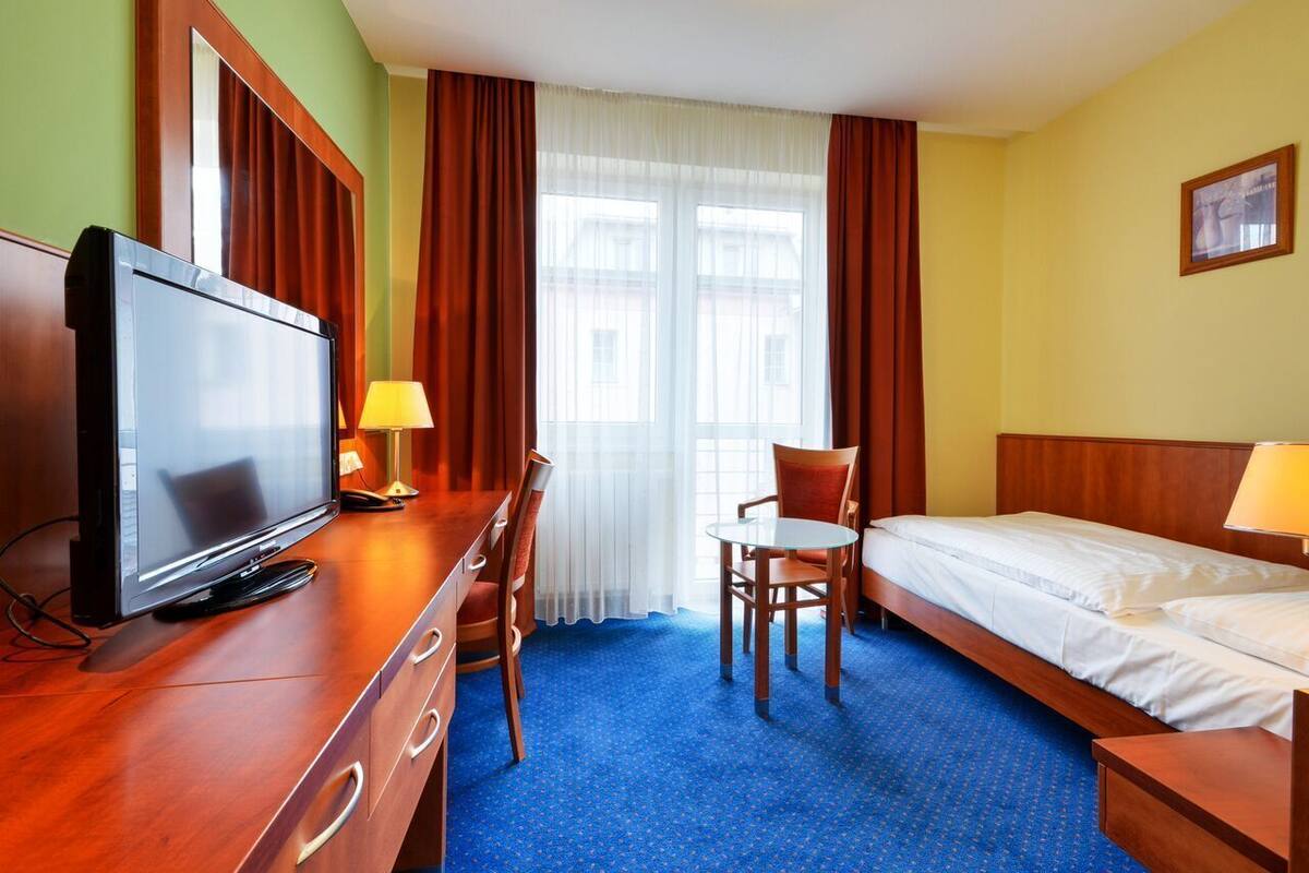 A hotel room with a TV, a desk, a chair, a bed, and a window with curtains.