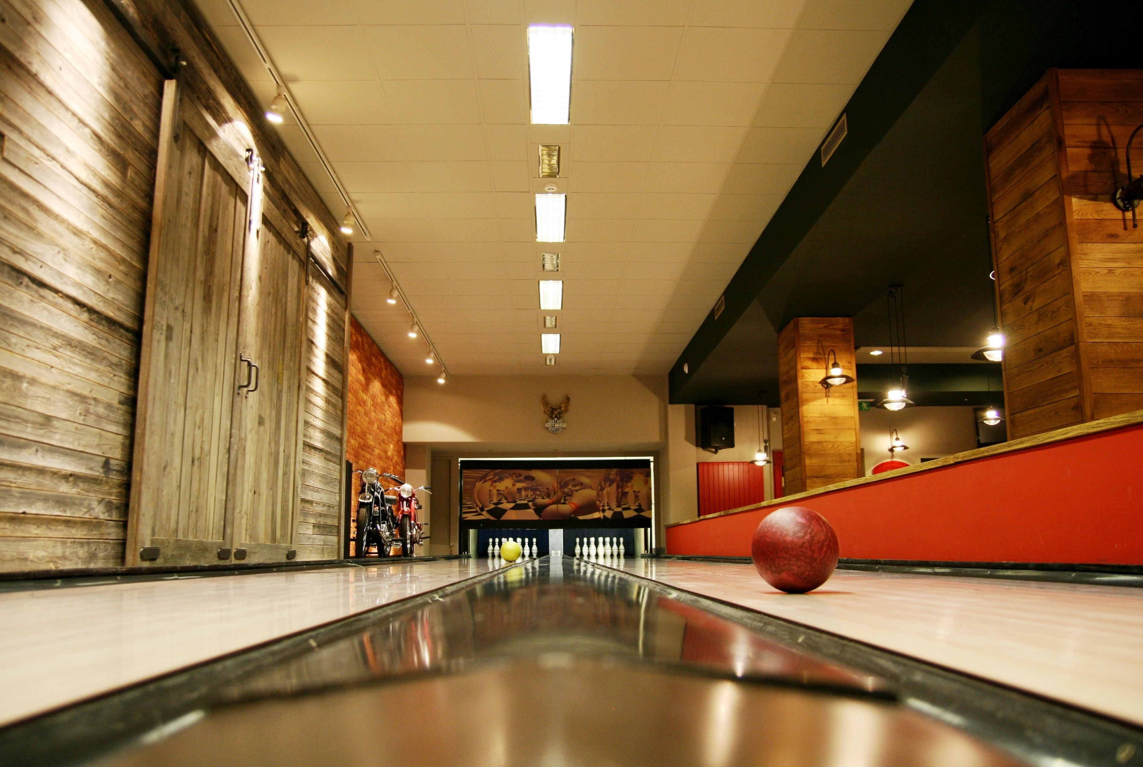 A bowling alley with a polished lane, wooden walls, and a red wall in the background.