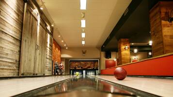 A bowling alley with a polished lane, wooden walls, and a red wall in the background.