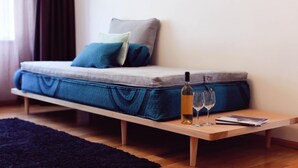 A bed with a mattress, pillows, a bottle of wine, two glasses, and a book on a wooden table.