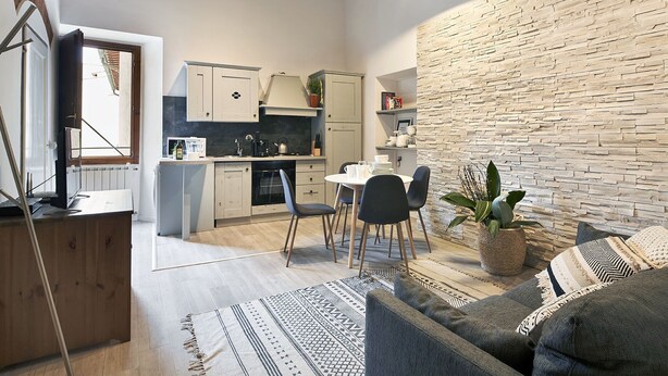 Una cocina moderna con armarios blancos, un comedor con mesa y sillas redondas, y una sala de estar con sofá y alfombra estampada.