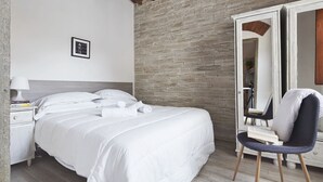 Un dormitorio con cama, mesita de noche, silla, espejo e imagen en la pared.