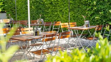 Un área de comedor al aire libre con mesas y sillas, rodeada por un seto.