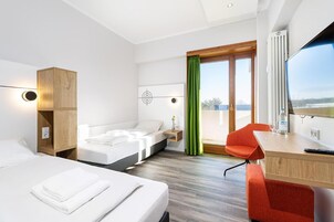 A hotel room with a bed, a desk, a chair, a window with a view, and a green curtain.