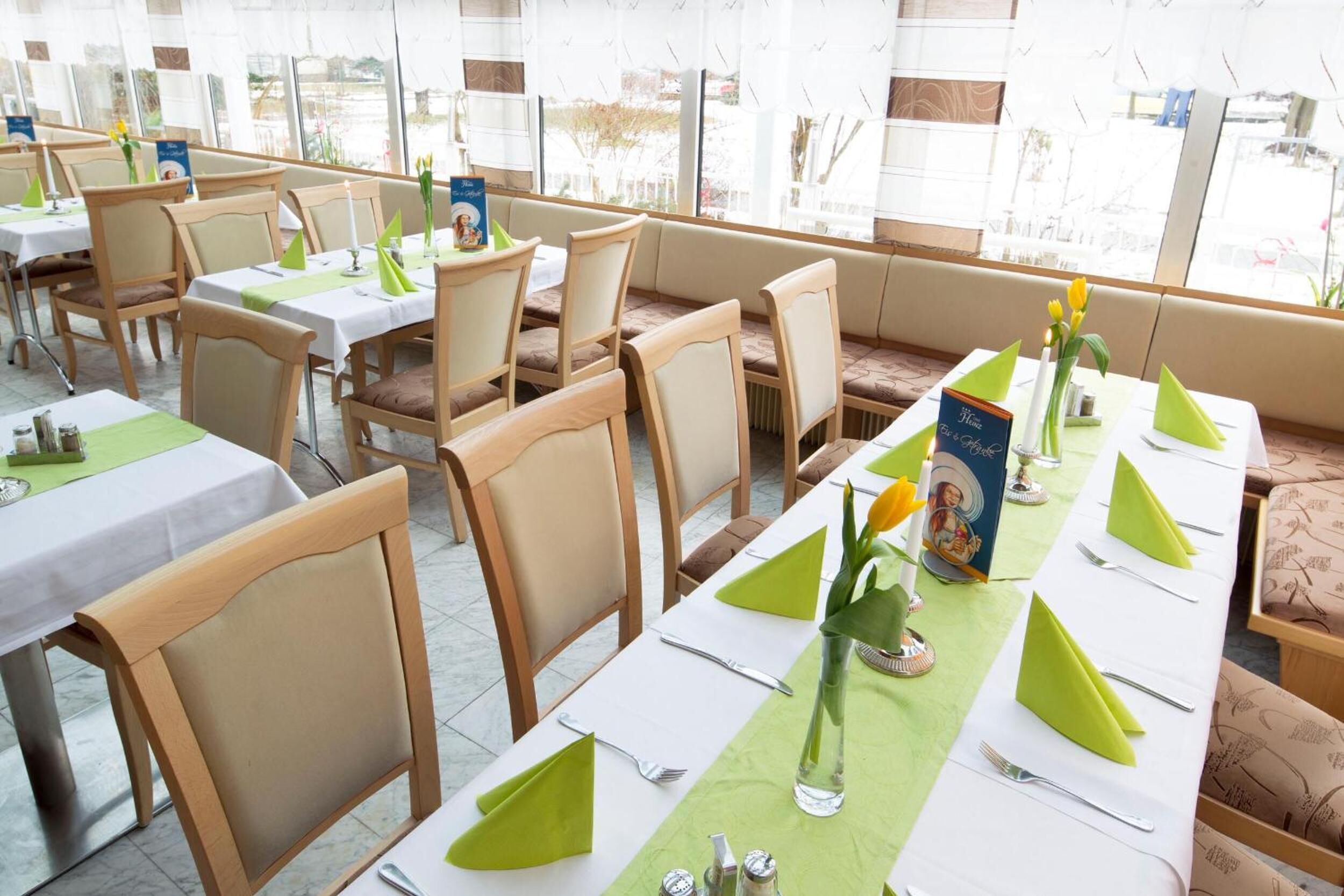 Una sala ristorante con diversi tavoli apparecchiati, con tovaglioli verdi, tovaglie bianche e posateria.