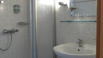 A bathroom with a glass shower enclosure, a sink with a mirror above it, and a toilet with a roll of toilet paper on it.