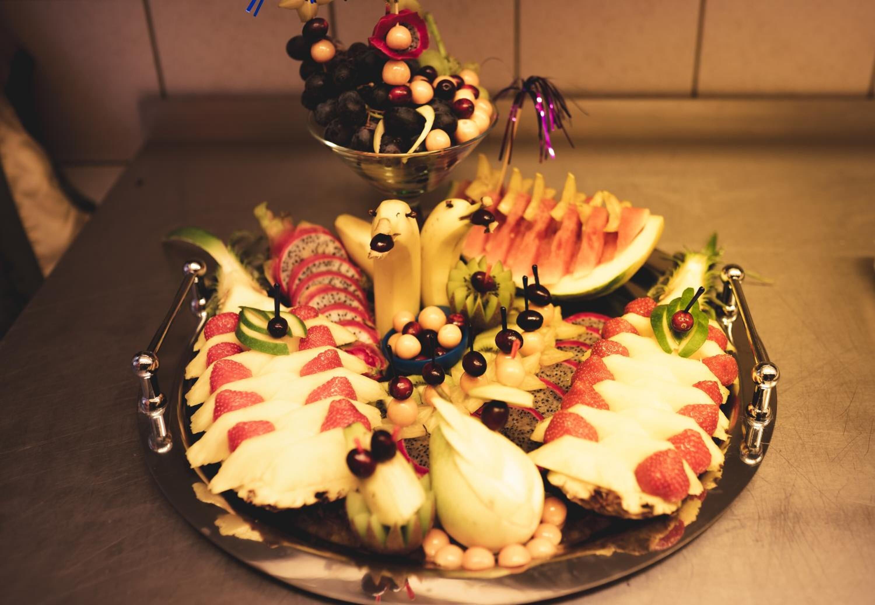 Una bandeja de frutas con diversas frutas y un cuenco decorativo sobre una mesa.