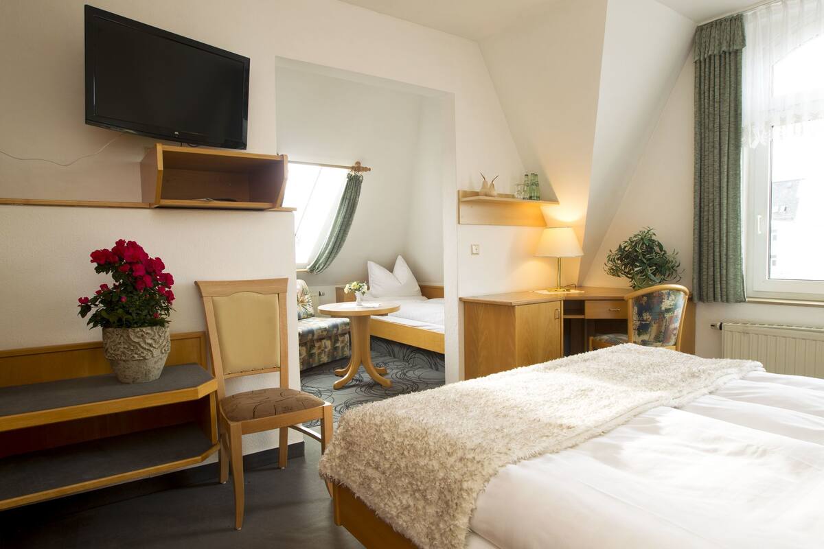 A hotel room with a bed, a desk, a chair, a TV, and a window with curtains.