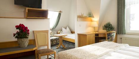 A hotel room with a bed, a desk, a chair, a TV, and a window with curtains.