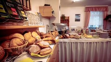 Un bufé con diferentes panes y pasteles, una estación de café y un comedor con mesas y sillas.