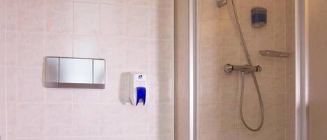 Un baño moderno con inodoro, ducha, lavabo y estante con artículos de aseo.
