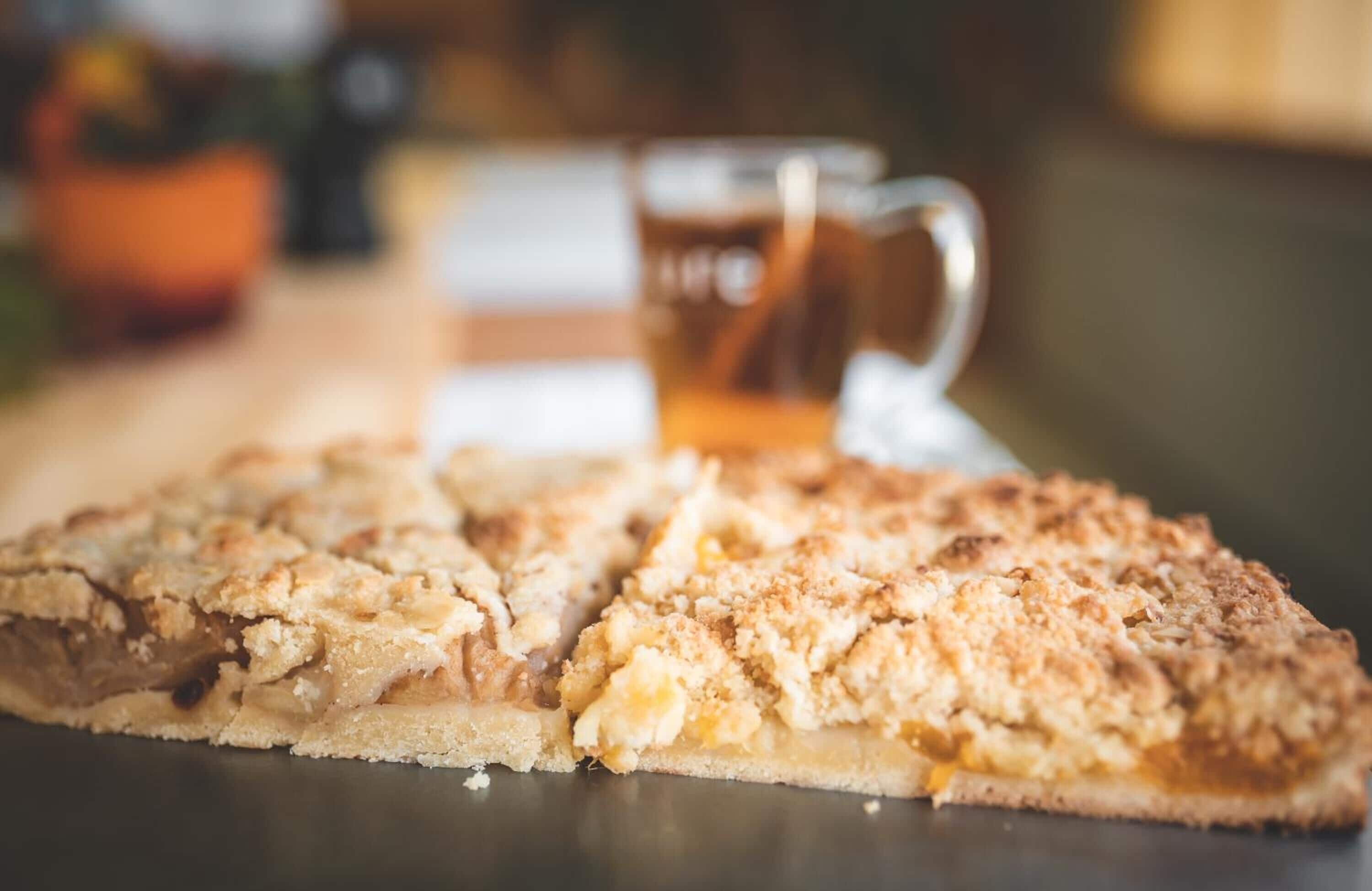 Ein Stück Apfelkuchen mit Streuseln auf einer dunklen Unterlage, unscharfer Hintergrund.