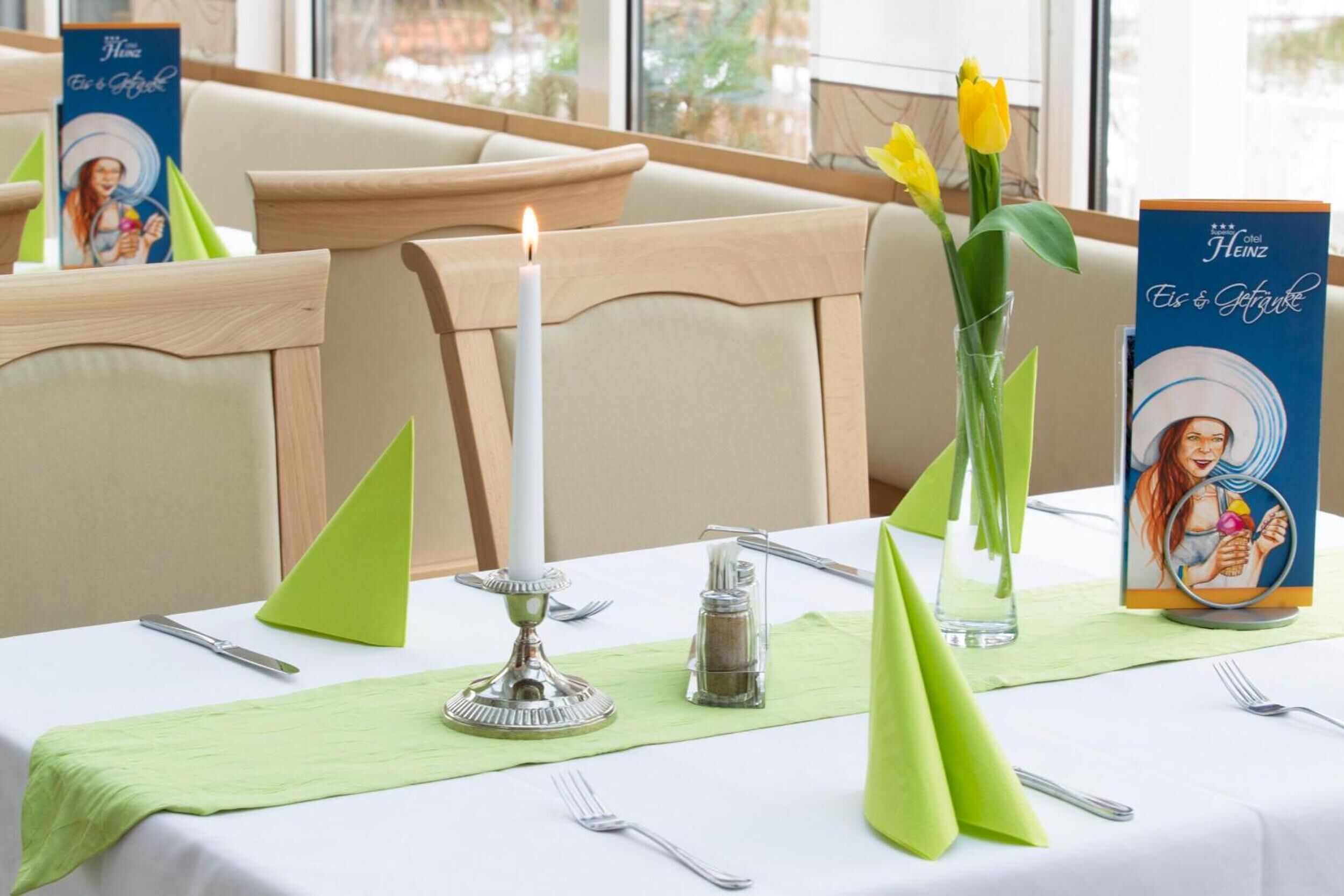 A dining table set with a candle, a salt shaker, a vase with flowers, and a menu stand.