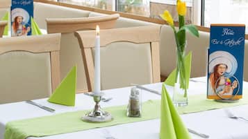 A dining table set with a candle, a salt shaker, a vase with flowers, and a menu stand.