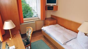 A hotel room with a bed, desk, chair, TV, and a window with curtains.