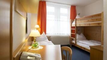 A hotel room with a bunk bed, a desk with a telephone, a lamp, and a window with curtains.