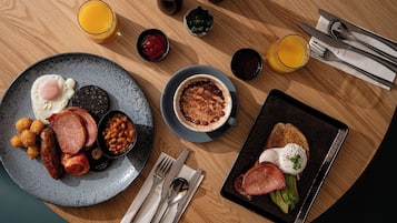 A breakfast setting with a plate of eggs, sausages, beans, and toast, along with a bowl of soup and a glass of orange juice.
