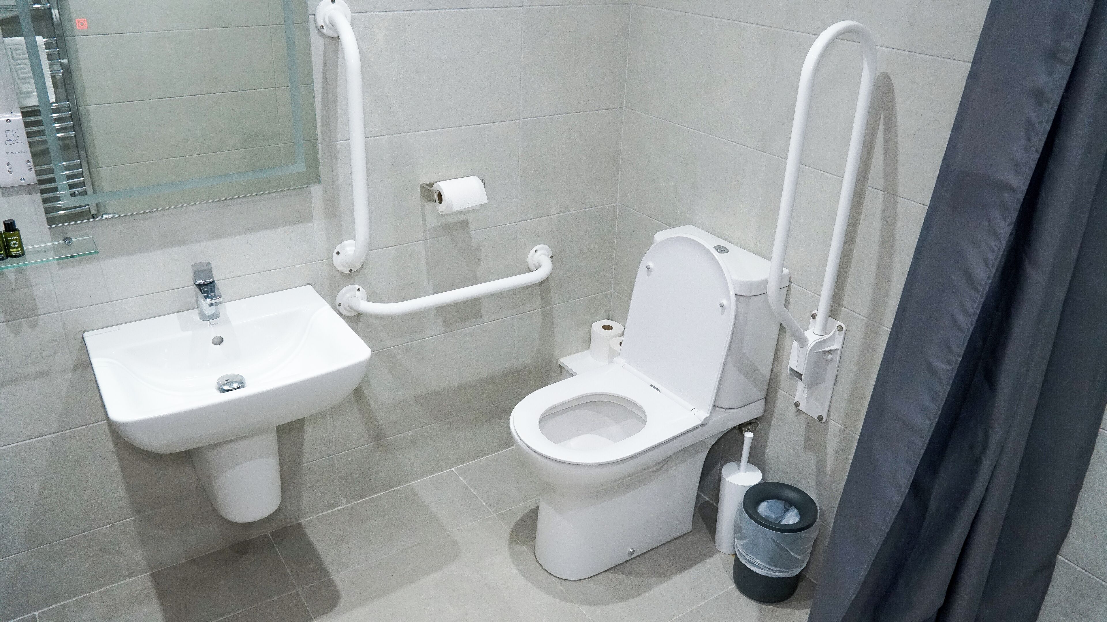 A modern bathroom with a white sink, toilet, and grab bars.