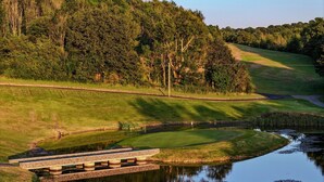 Un campo de golf con un estanque, un puente y una colina boscosa.