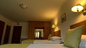 Habitación de hotel con una cama grande, un escritorio y un espejo. Se ve una ventana con cortinas y una puerta a la izquierda.