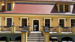 A yellow building with a red roof, a central entrance, and outdoor seating areas. - Pałac w Rymaniu (Ryman)