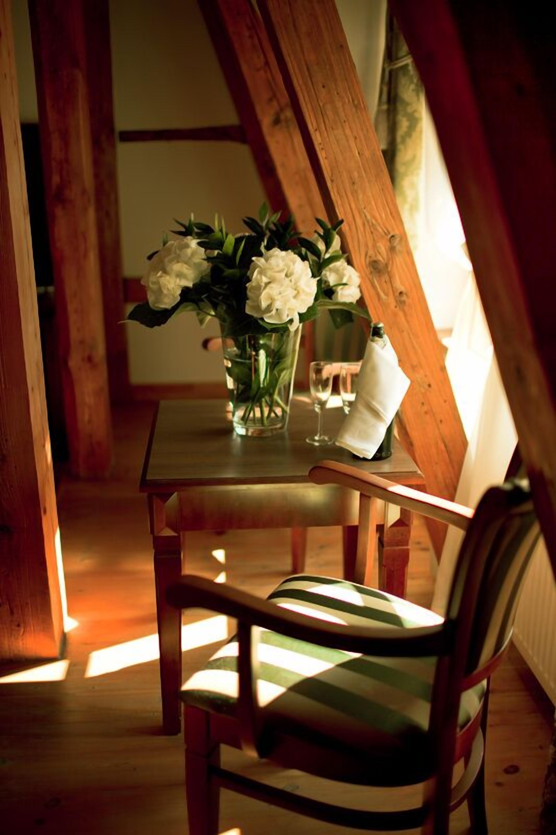 A wooden table with a vase of white flowers and a glass of water.